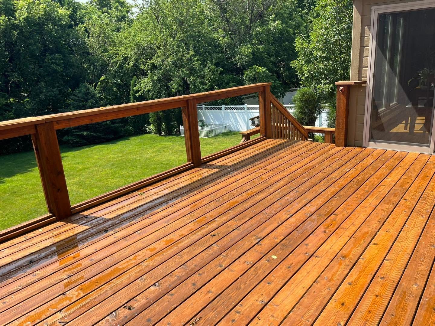 Wooden deck with railing overlooking a green backyard and trees, beside a house.
