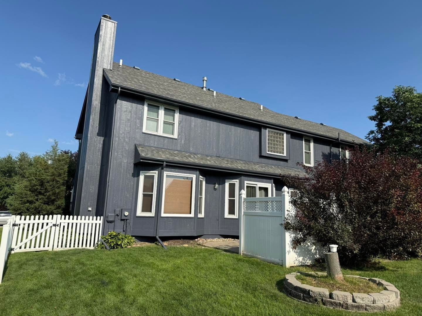 Dark gray two-story house with white trim, small fenced yard, and a blue gate under a clear sky