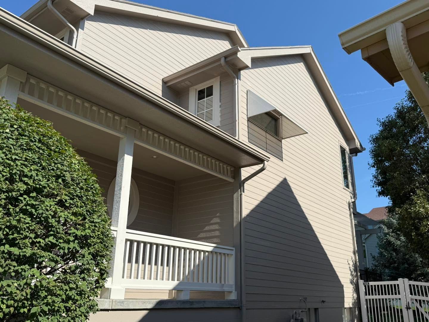 Beige townhouse exterior with white trim, porch, and hedges under a clear blue sky