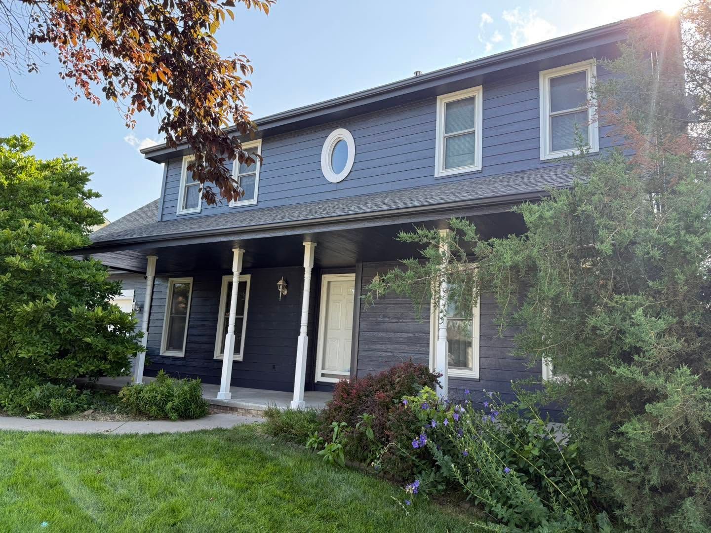 Two-story navy house with white trim, front porch, and a garden in bright sunlight.
