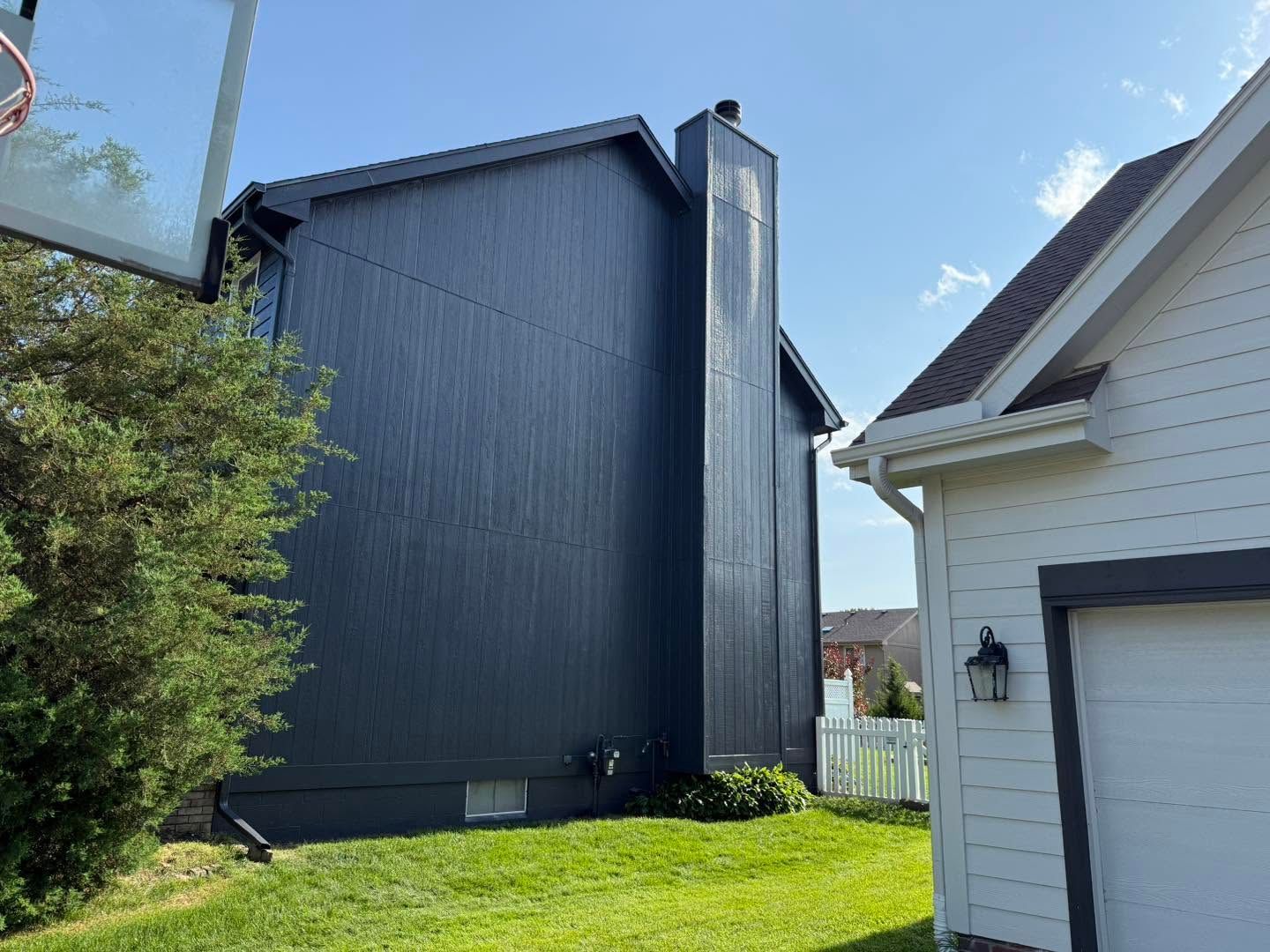 Tall dark-blue house beside a white garage in a sunny suburban yard