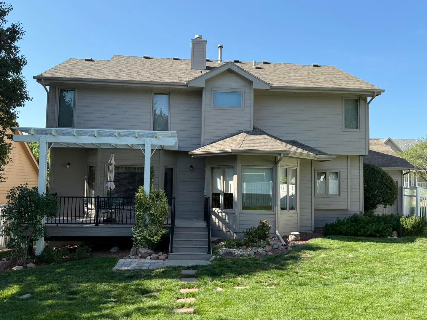 Two-story beige house with front porch, stairs, and green lawn under a clear blue sky