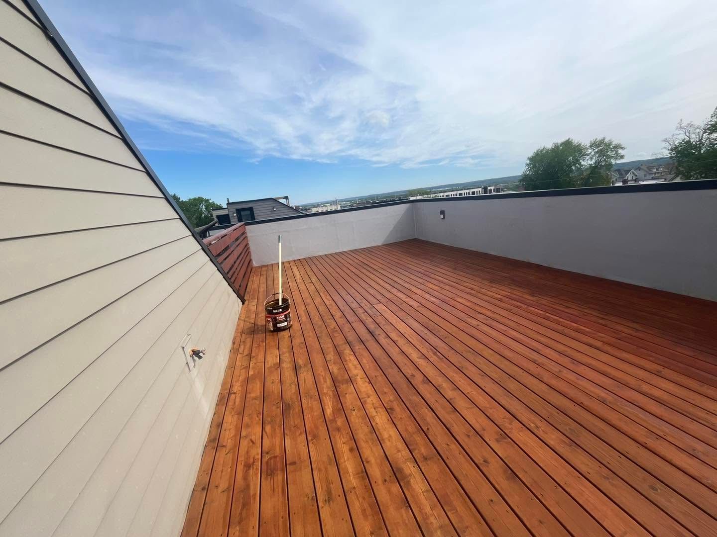 Wooden rooftop deck with gray walls and blue sky, viewed along the length of the terrace.