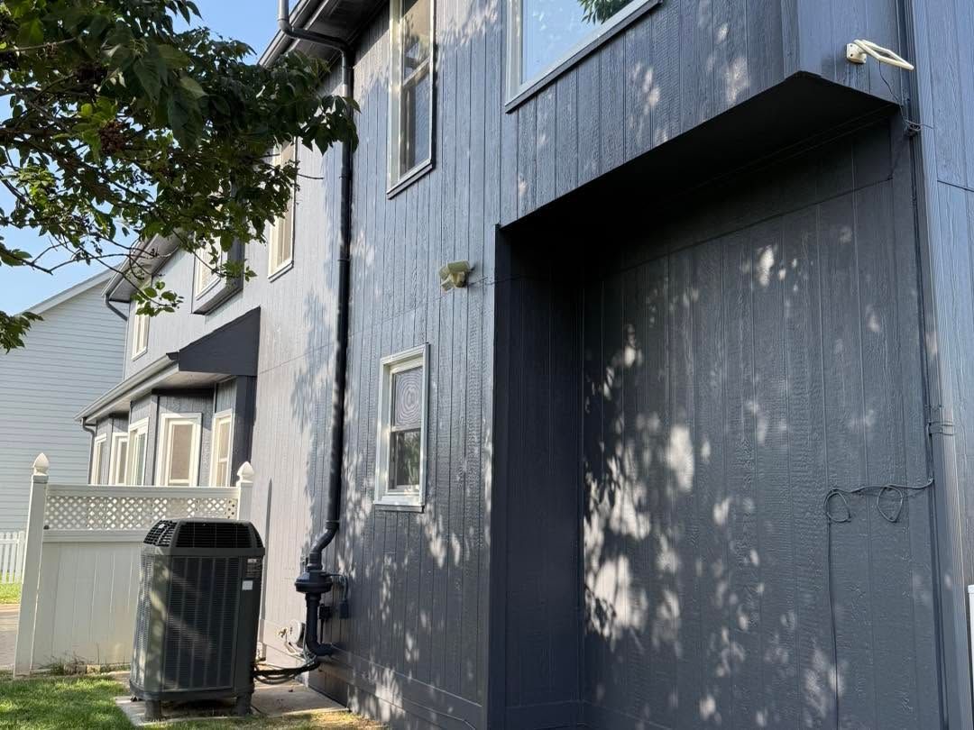 Dark blue house exterior with a fenced side yard and trash bin under tree shadows