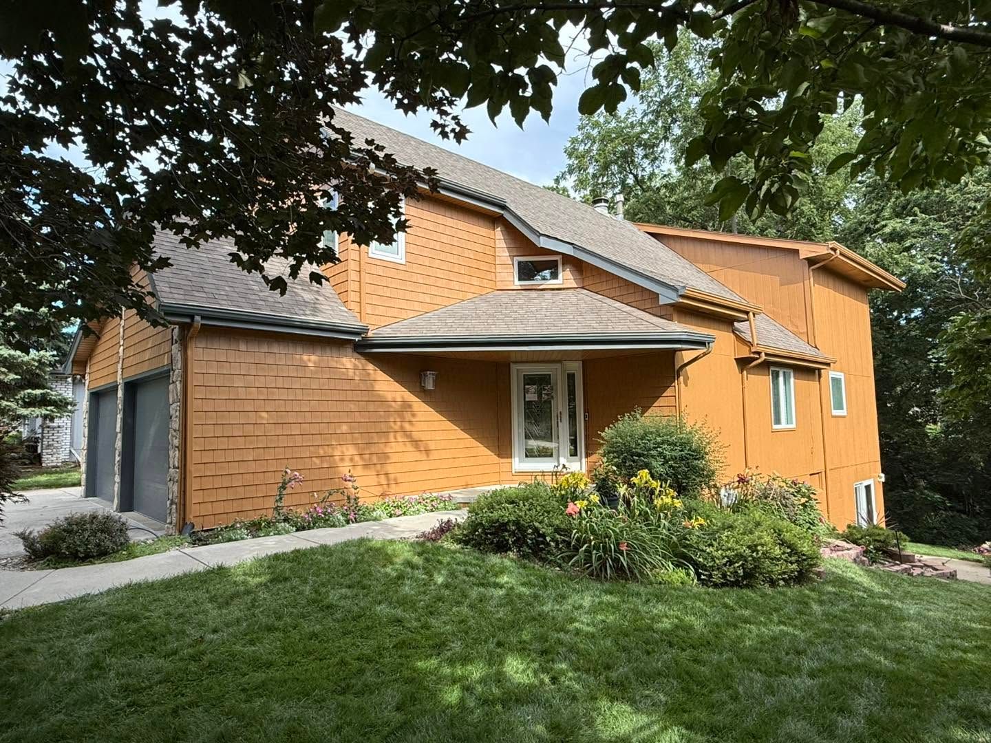 Orange house with brick siding, gray roof, and green lawn surrounded by trees