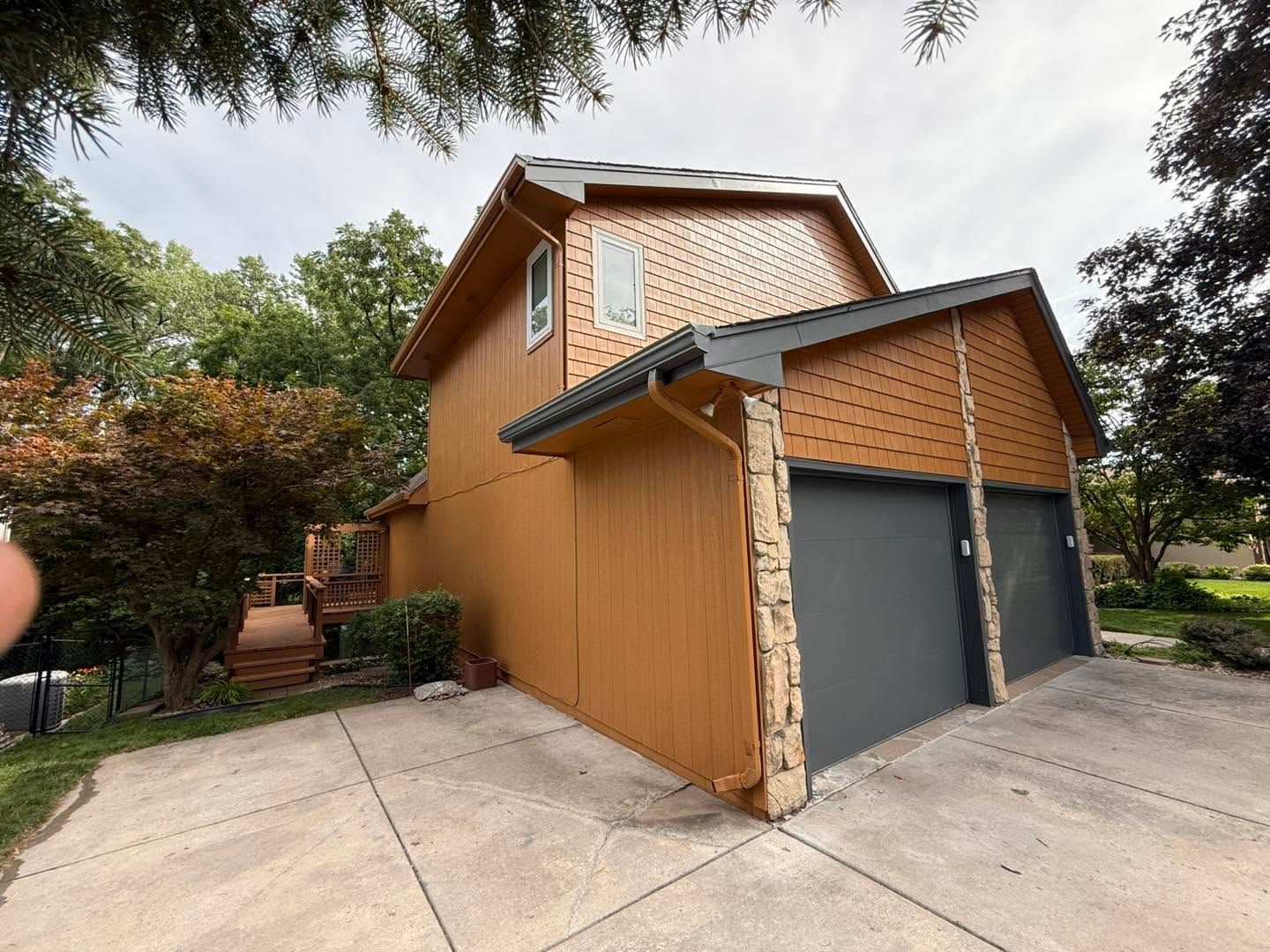 Side view of a tan garage with dark doors, concrete driveway, and trees overhead