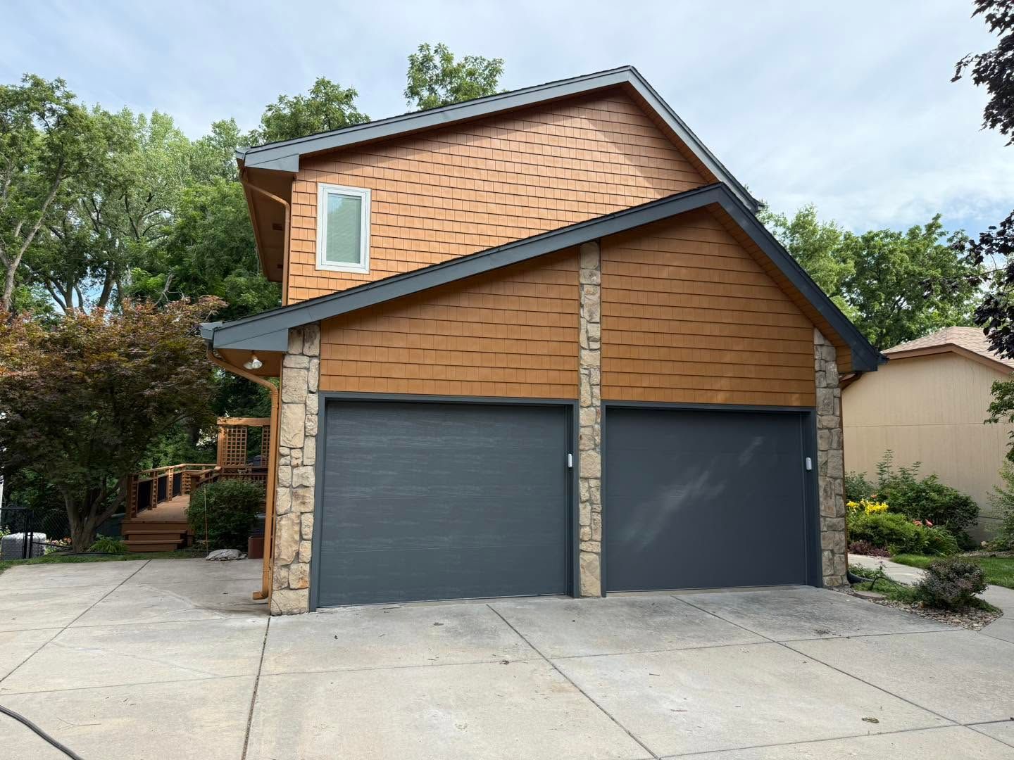 Two-story house with tan siding and a double dark gray garage door, viewed from the driveway.