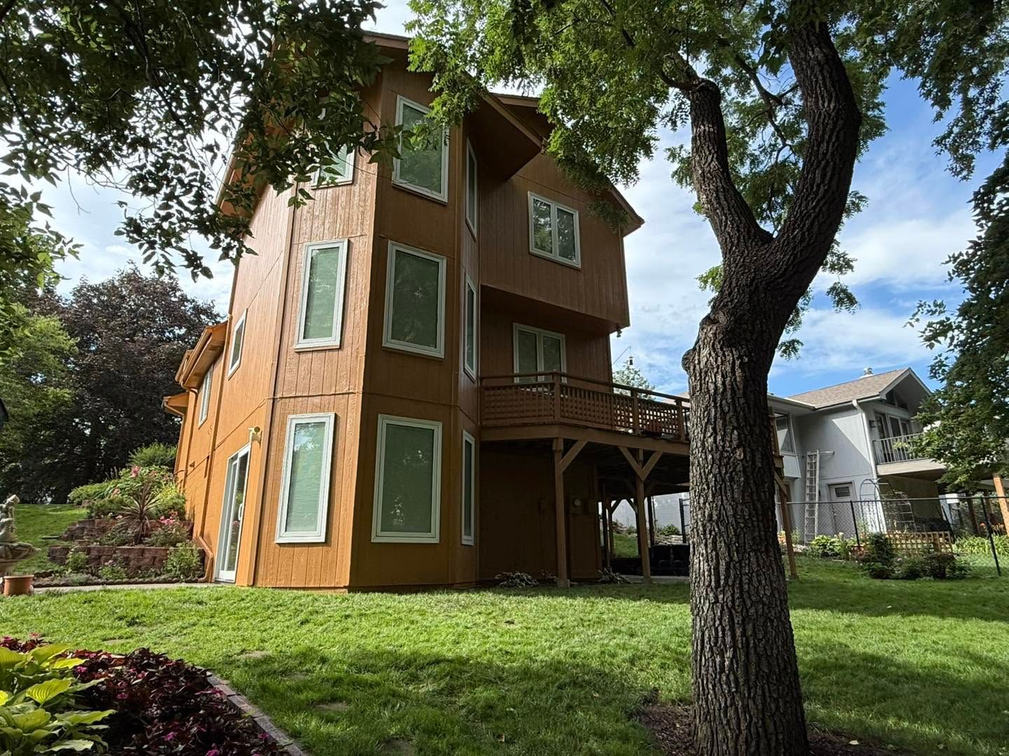 Tall narrow orange house with green-trimmed windows in a grassy yard, framed by large trees and a blue sky.