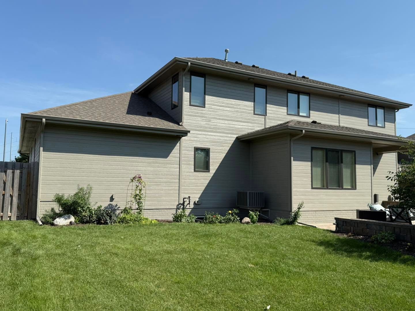 Two-story beige house with a sloped roof and green lawn under a clear blue sky