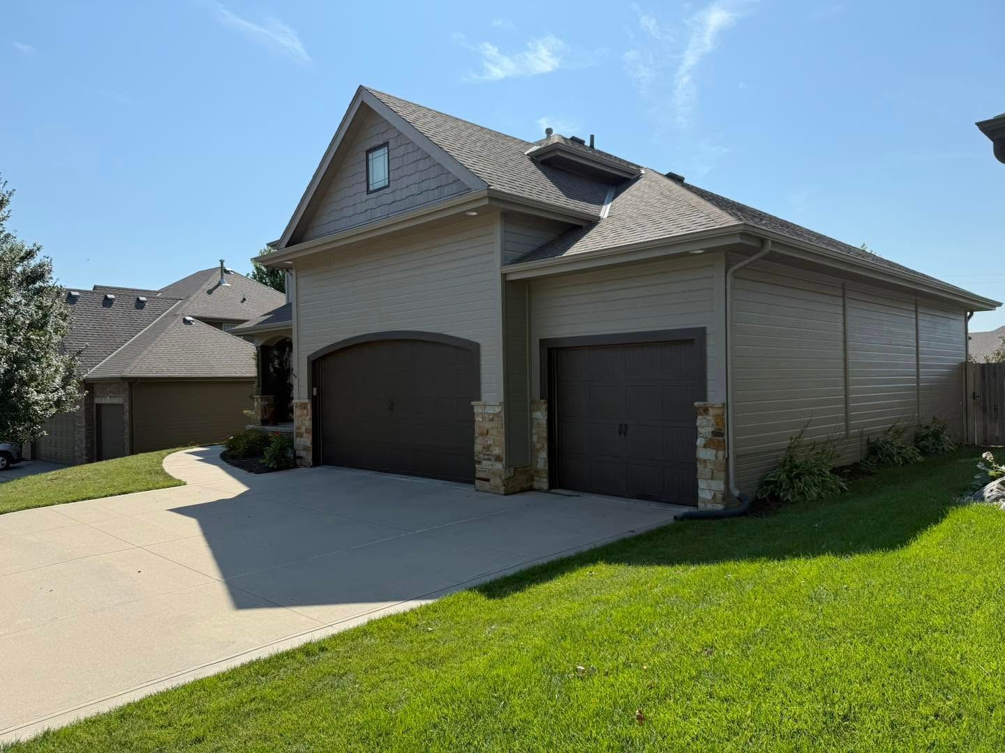 Suburban house with two garage doors, light siding, and a sloped driveway under a bright blue sky