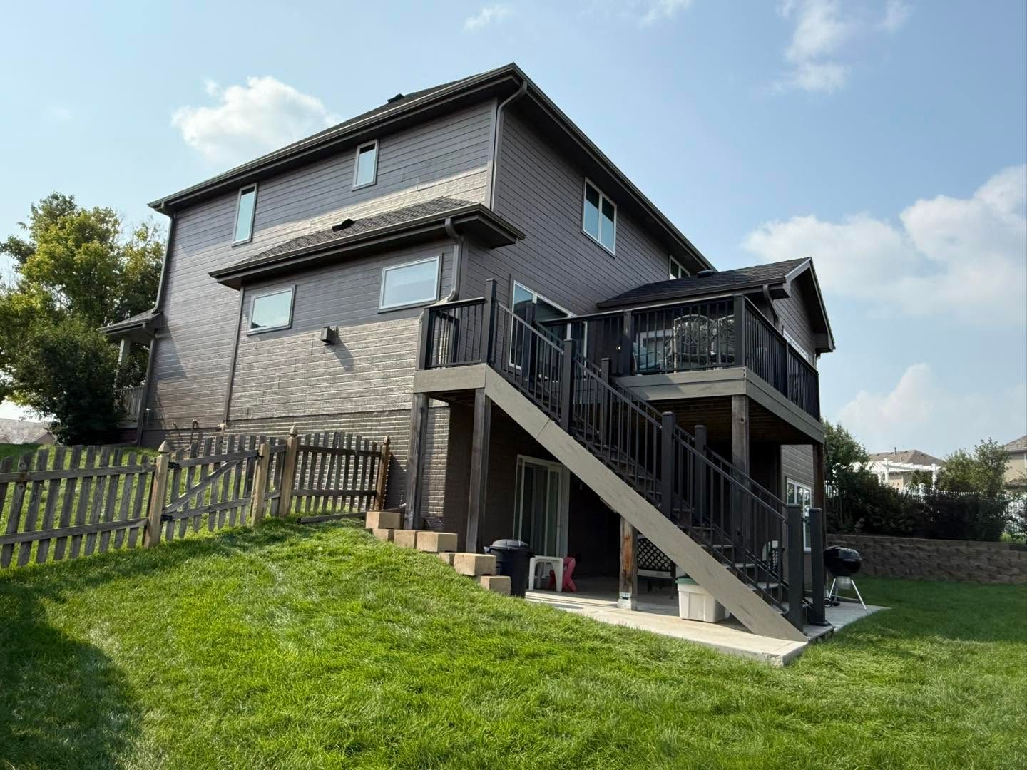 Two-story house with an exterior staircase, fenced lawn, and blue sky.