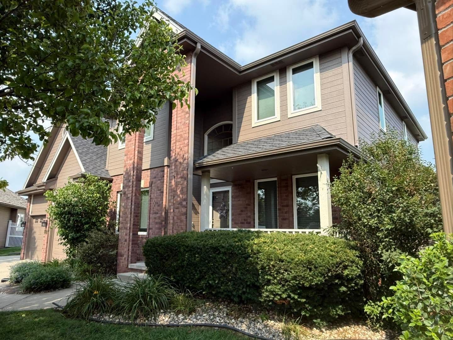 Two-story suburban house with brick and tan siding, front porch, and trimmed hedges