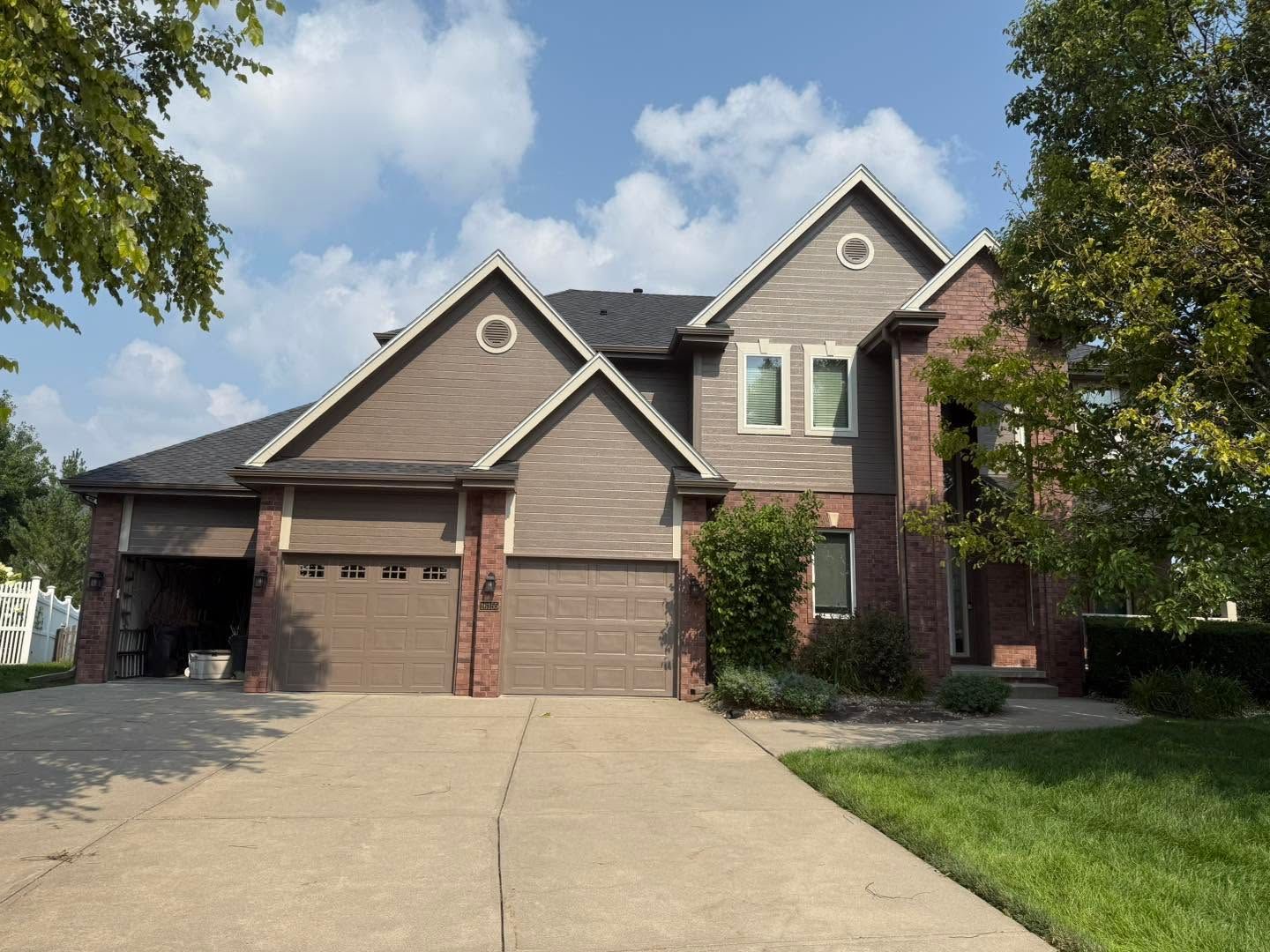 Suburban brick house with a two-car garage and a long driveway under a partly cloudy sky