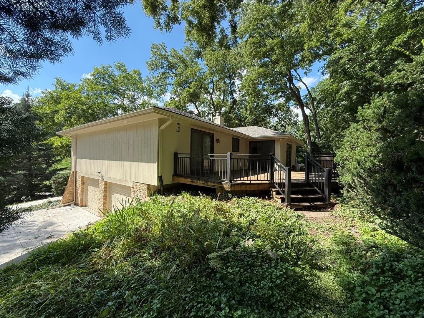 Single-story beige house with porch and steps, surrounded by trees and bushes in a wooded setting
