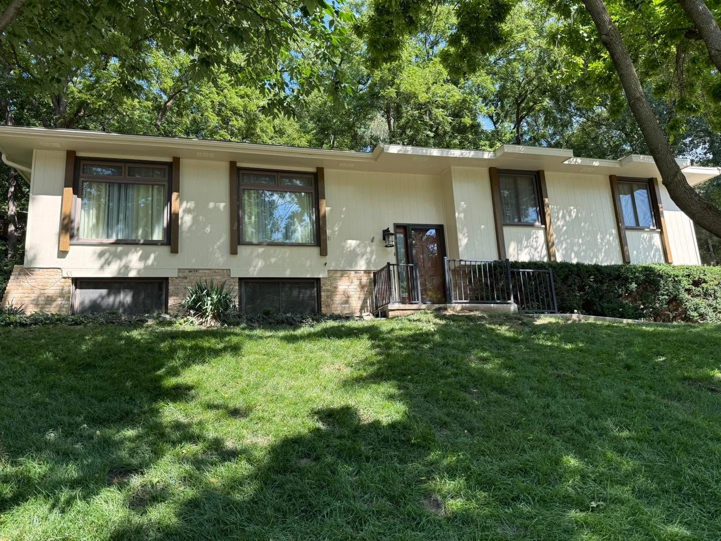 Single-story house with cream walls, green lawn, and large trees in the yard.