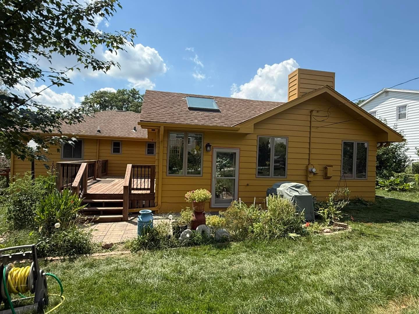 Yellow wooden house with a porch and garden, viewed from the yard on a sunny day