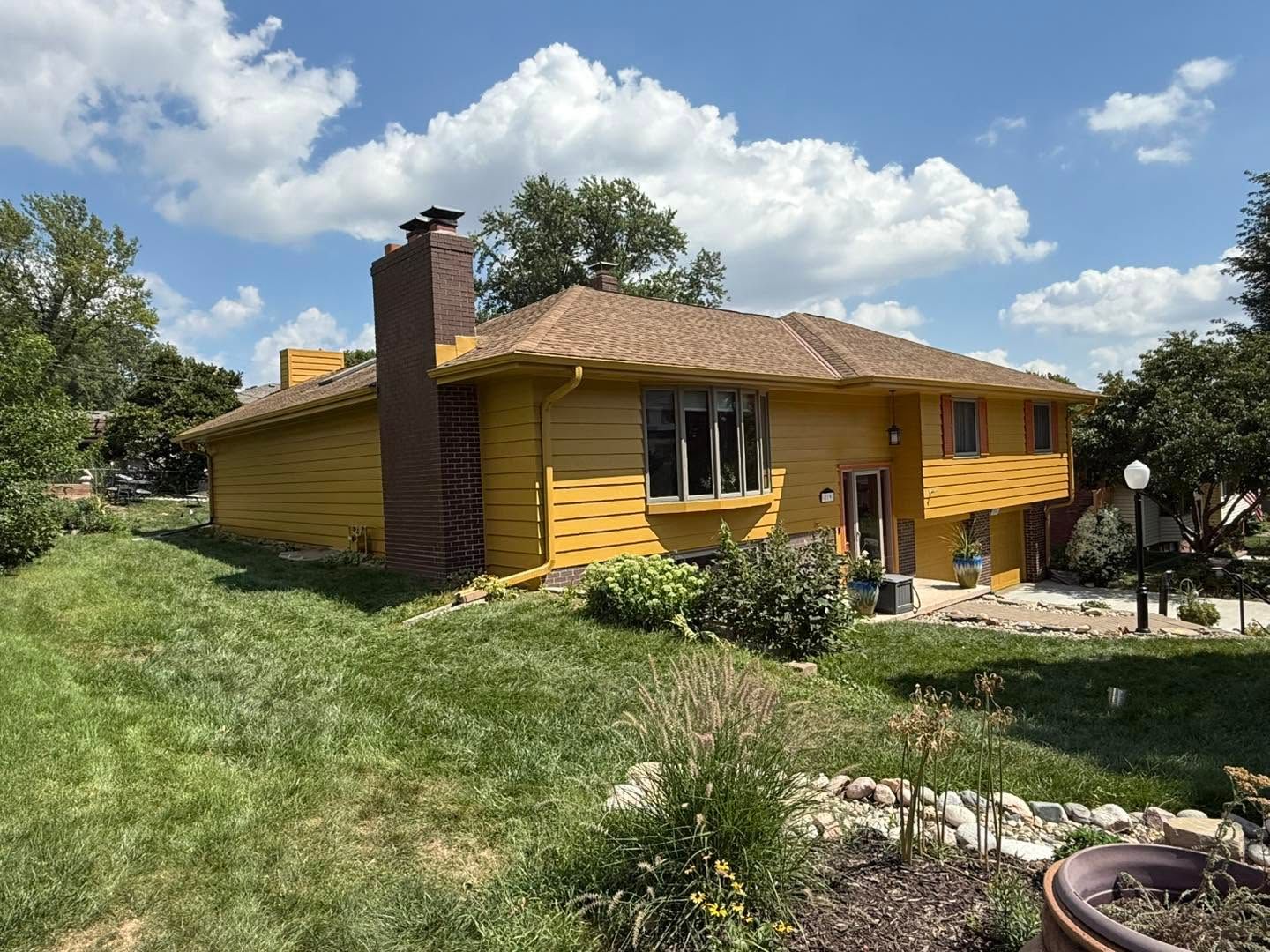 Yellow log-style house with a brick chimney and grassy yard under a partly cloudy sky
