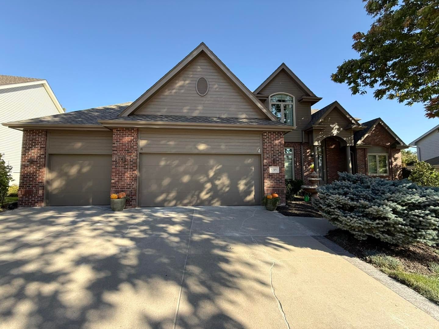 Suburban brick house with a two-car garage, peaked roof, and front porch in daylight