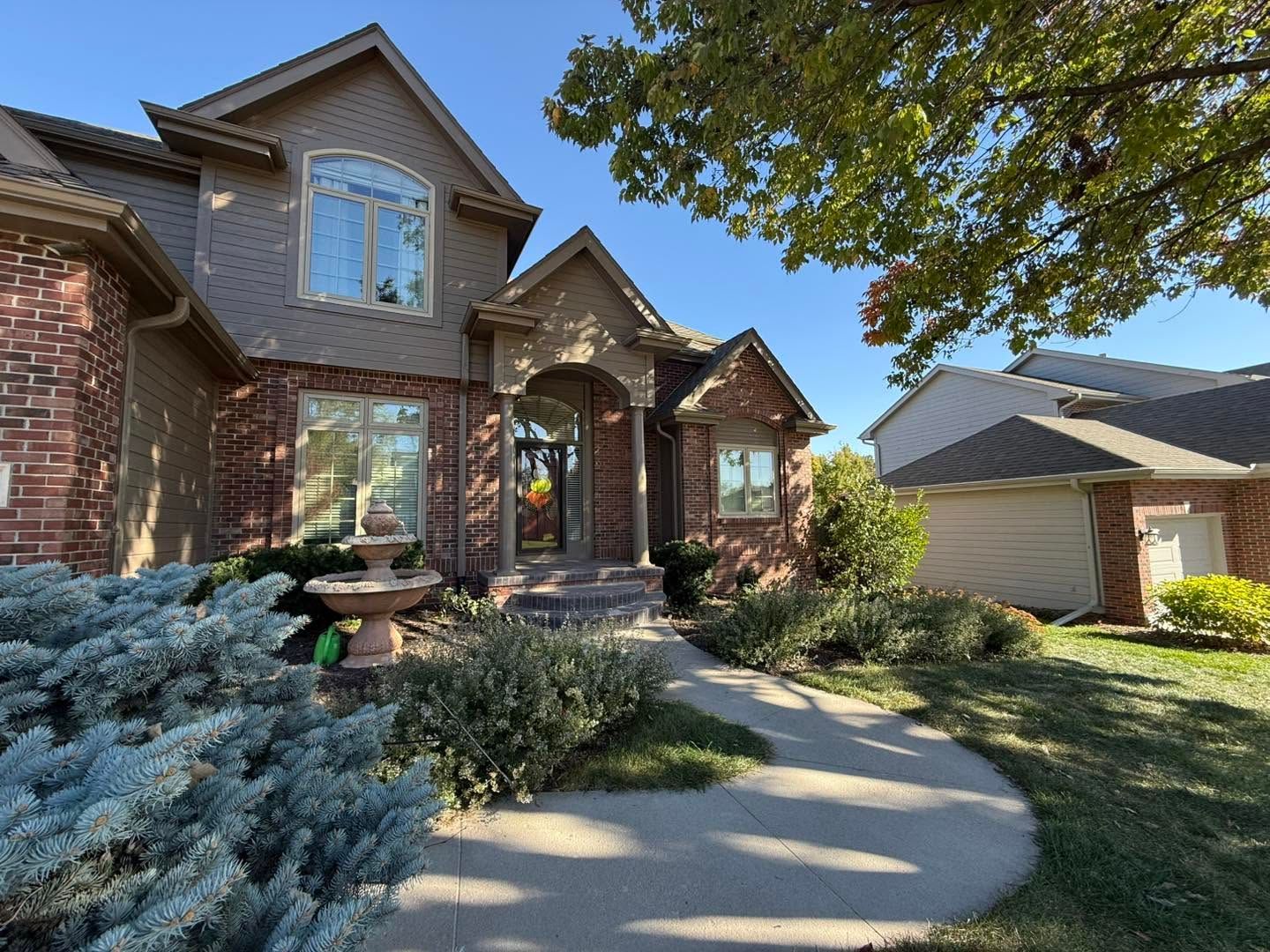 Brick suburban house with arched entry, curved walkway, and landscaped front yard under blue sky