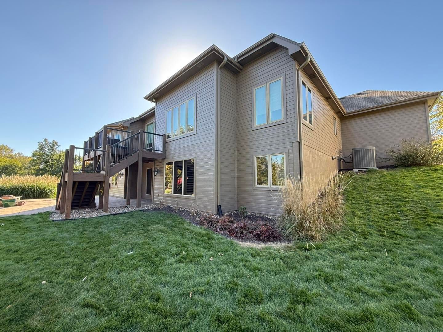 Suburban two-story tan house with deck and large windows, viewed from a grassy backyard
