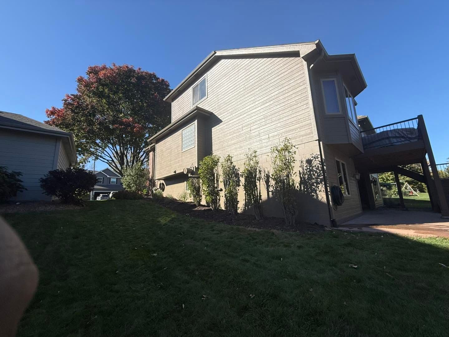 Residential building on a grassy slope with a tree, blue sky, and a carport on the right