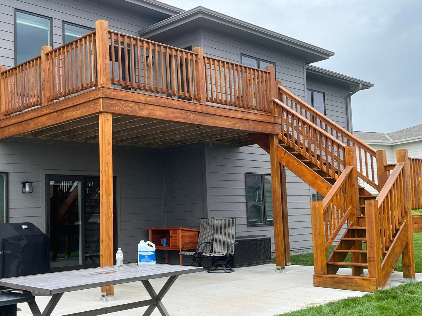 Wooden deck with stairs attached to a gray two-story house, with a covered patio below.