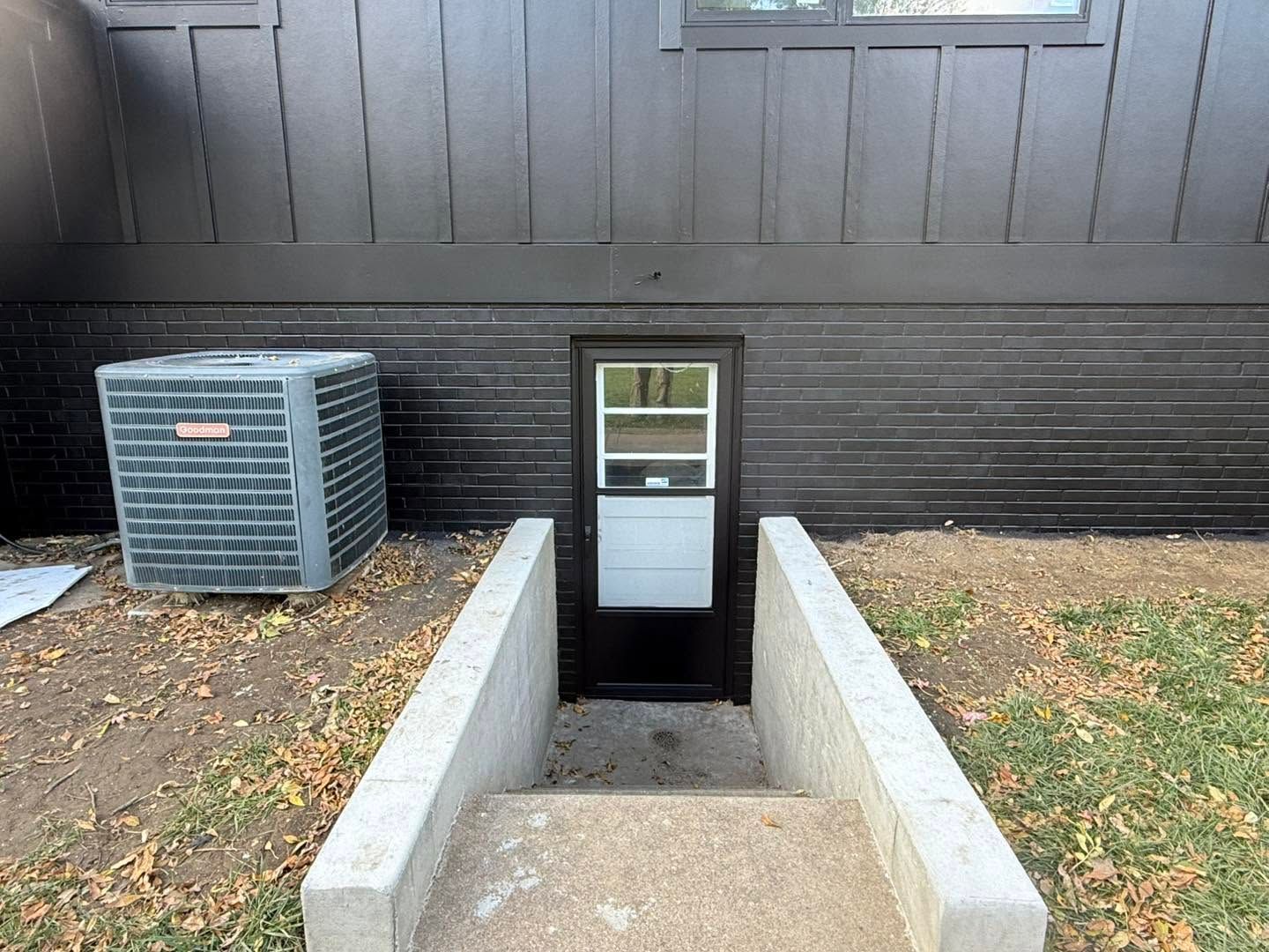 Basement stairwell entrance beside a house, with concrete walls and an outdoor AC unit.