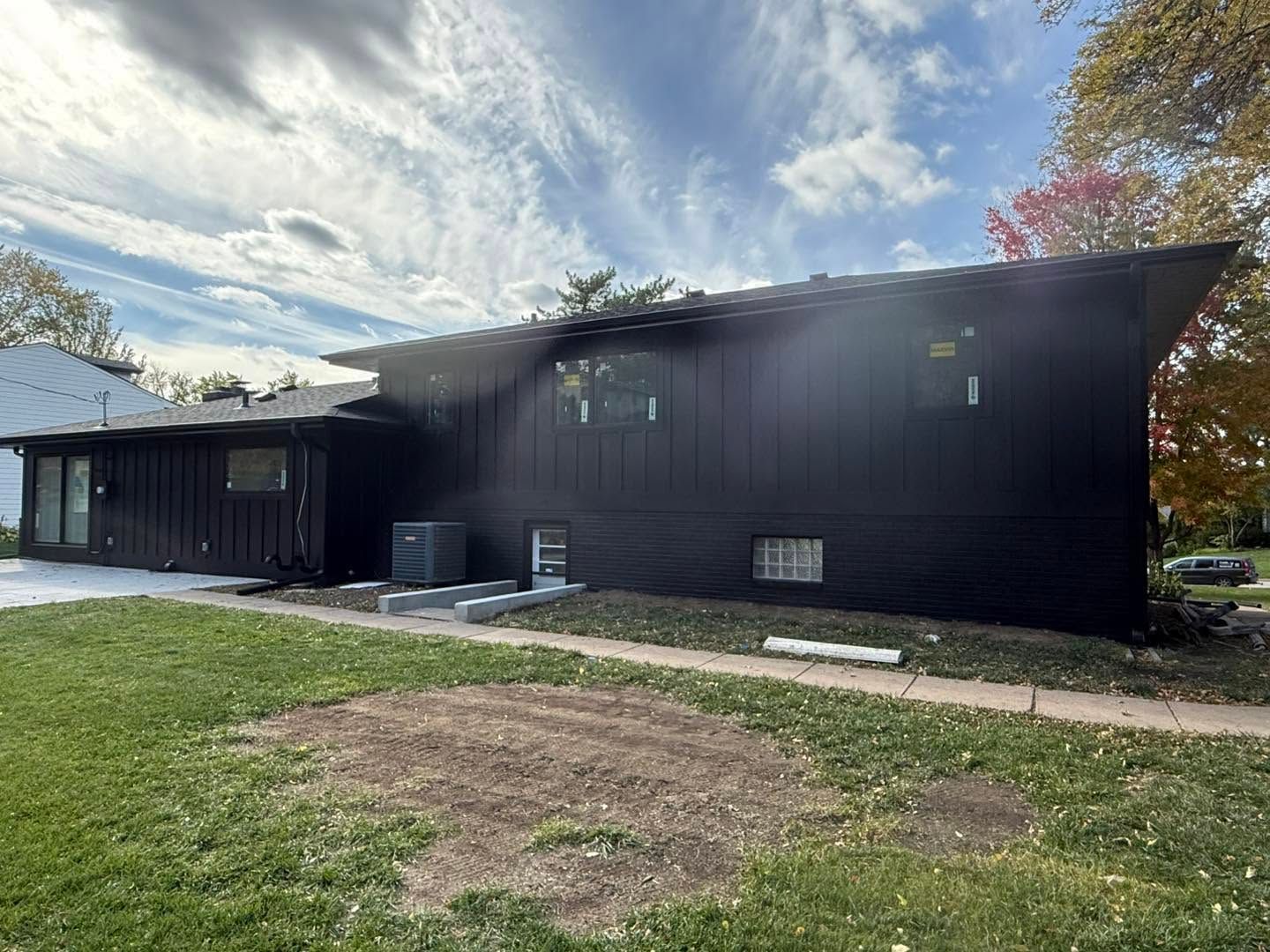 Black house exterior with sloped roof, small windows, and a grassy yard under a cloudy sky