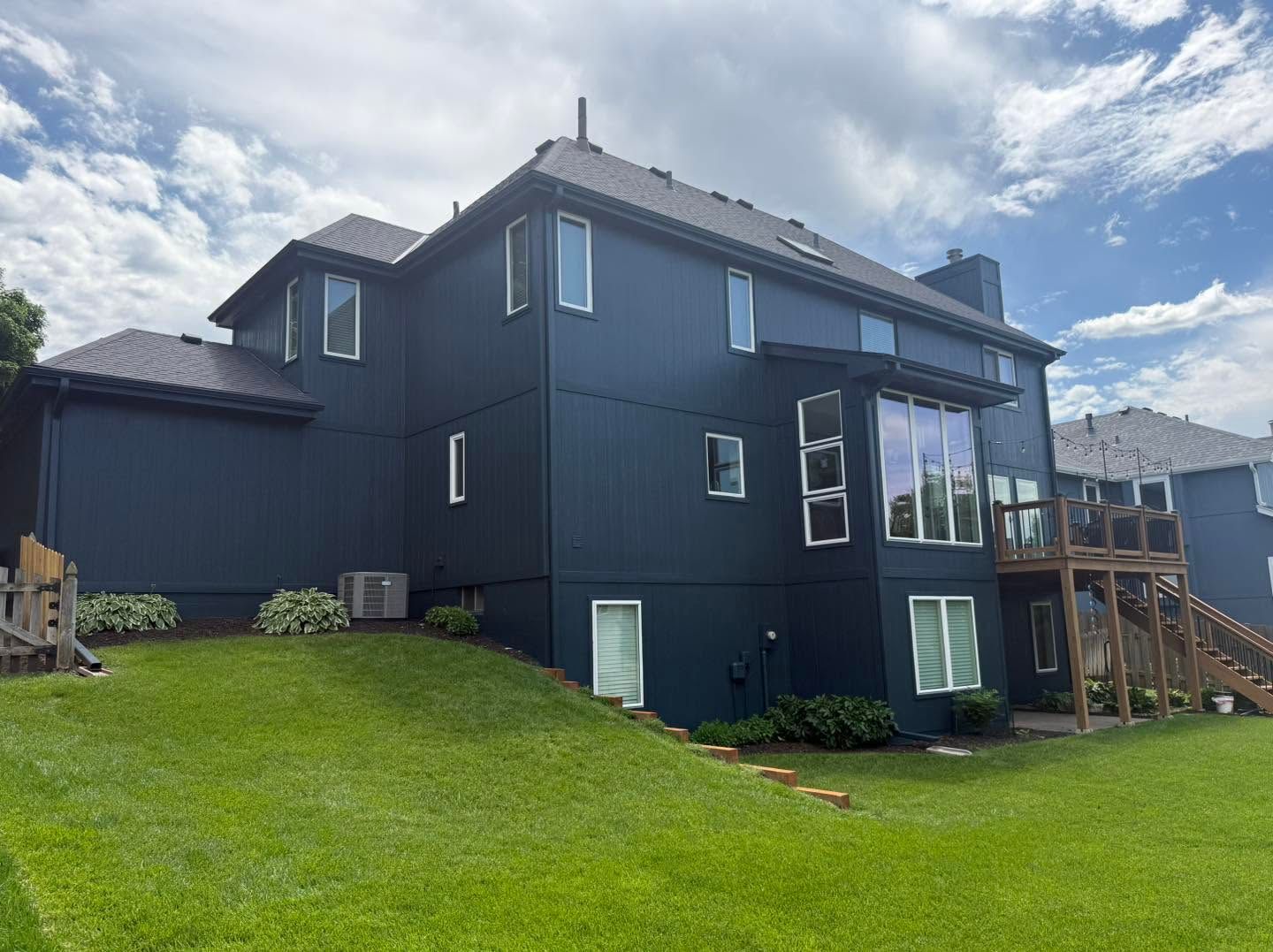 Black two-story house with large windows on a grassy hill under a cloudy sky