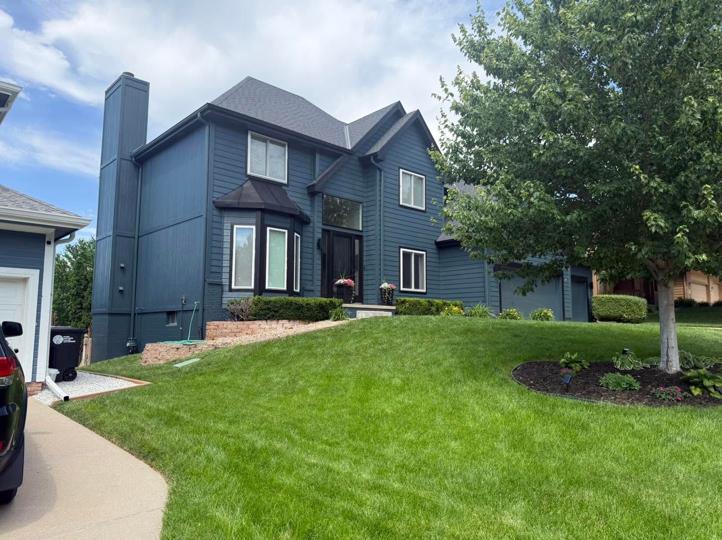 Dark blue two-story house with a sloped roof and green lawn under a cloudy sky