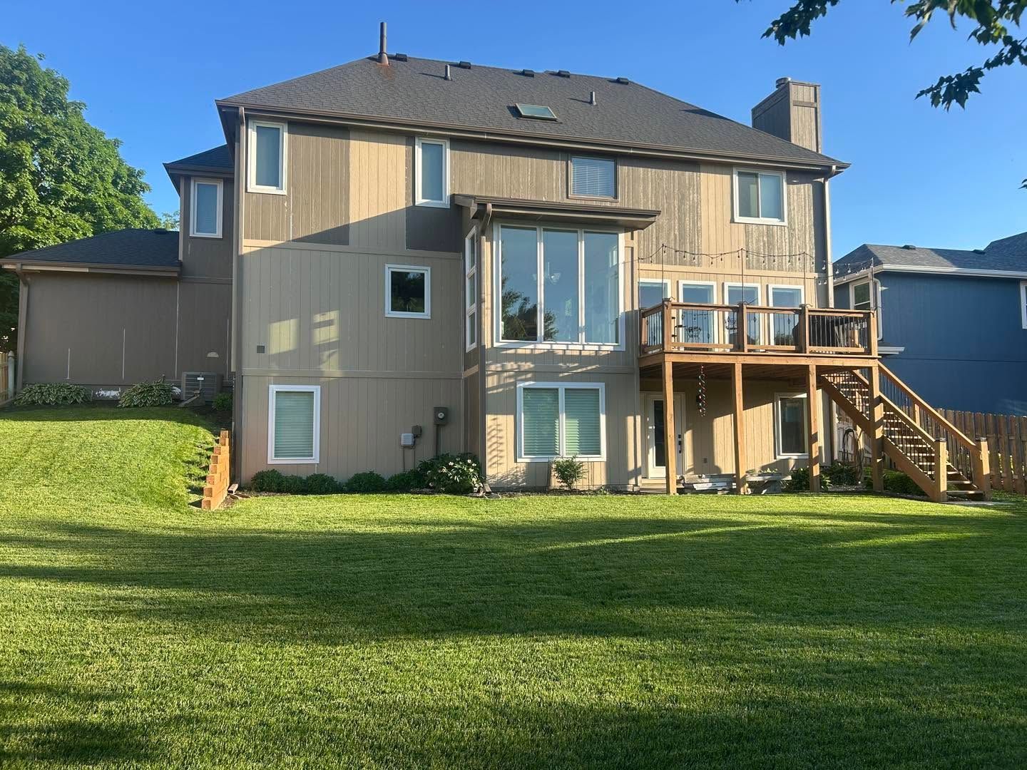 Backyard view of a two-story beige house with a wooden deck and large grassy lawn