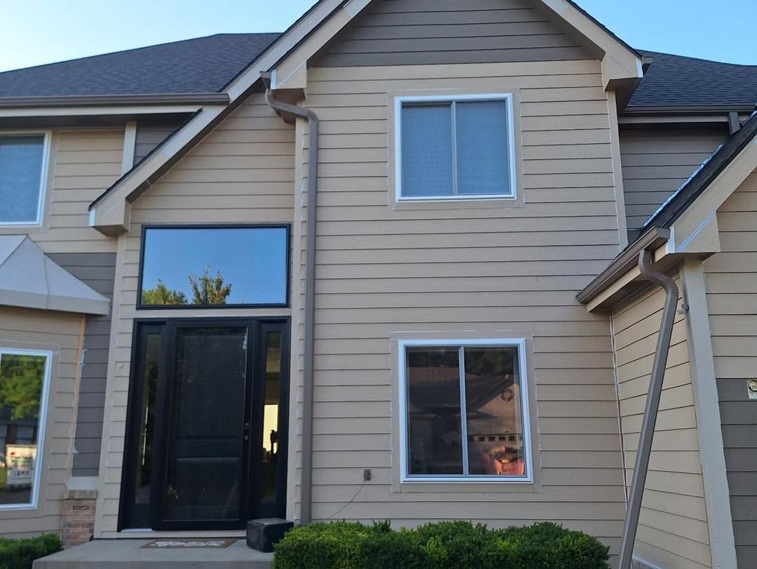Front entrance of a beige two-story house with black double doors and white-trimmed windows