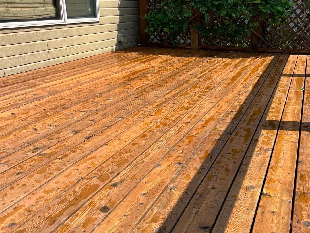 Sunlit wooden deck beside a beige house, with shadows from a railing across the boards.
