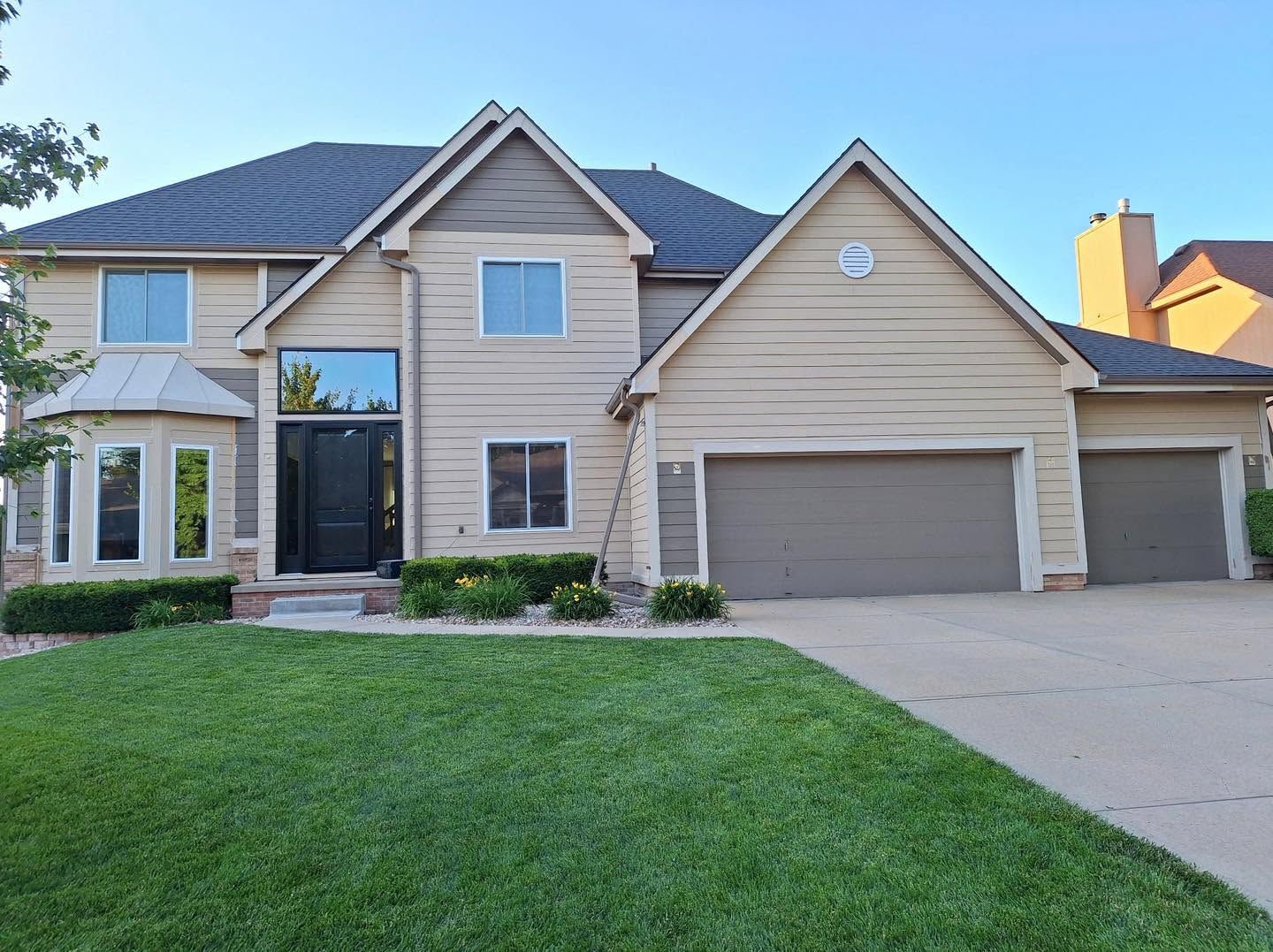 Two-story beige suburban house with a double garage and a green lawn in front