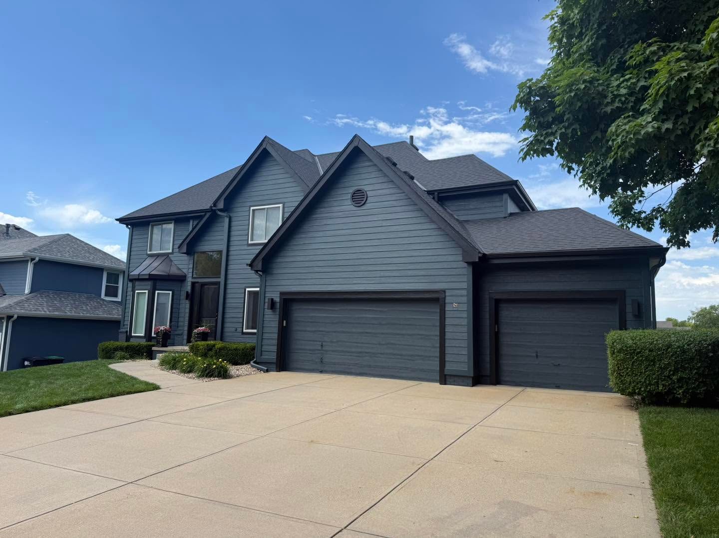 Two-story suburban house with a three-car garage and wide driveway under a blue sky