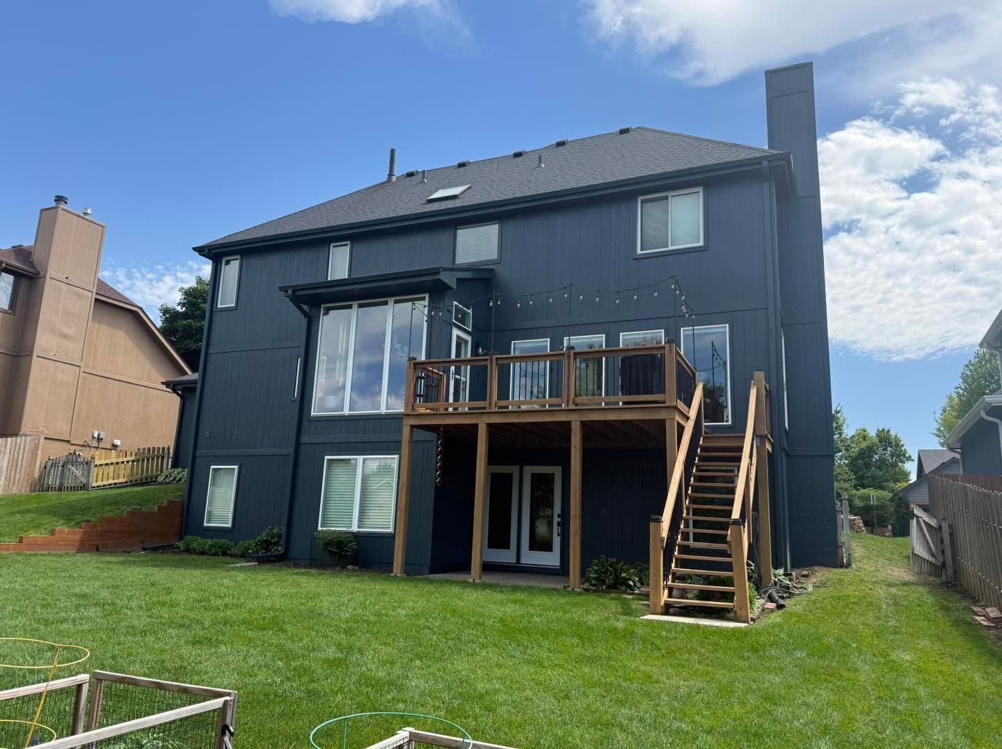 Back of a dark gray house with a wooden deck and stairs overlooking a grassy yard