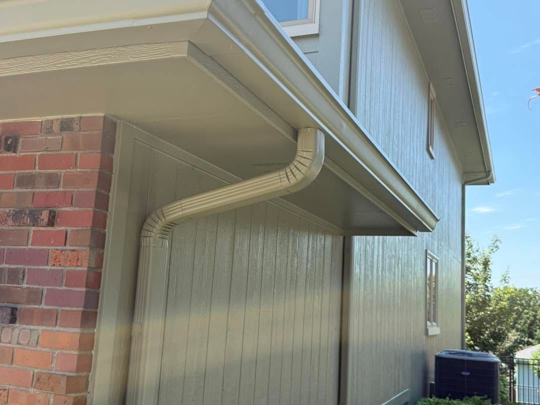 House exterior with brick wall, tan siding, and white gutter under the eaves