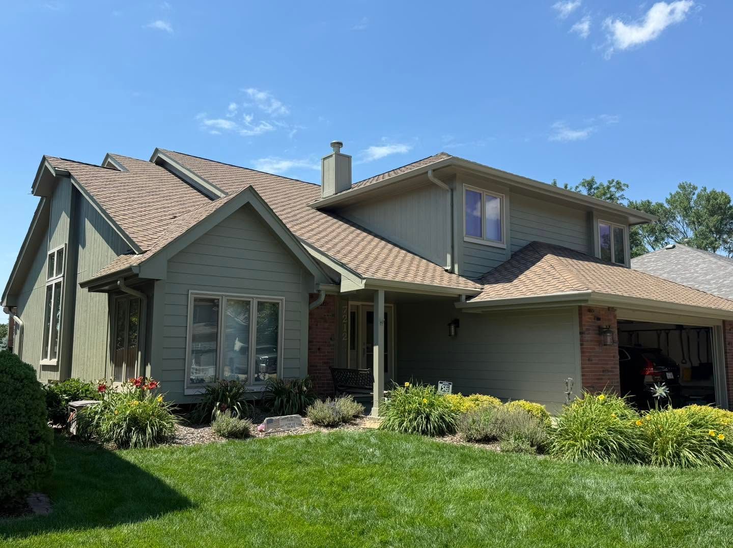 Suburban house with green lawn, gray siding, and a tan roof under a blue sky