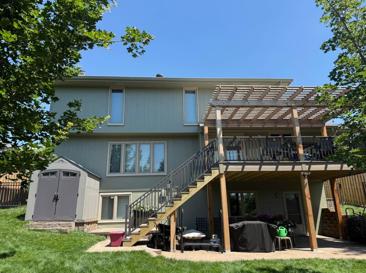 Two-story house with gray siding, exterior stairs, deck, and a tree in the yard under a clear blue sky