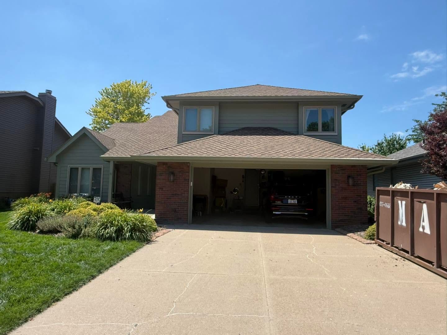 Suburban two-story house with brick facade, wide driveway, and attached garage under a blue sky