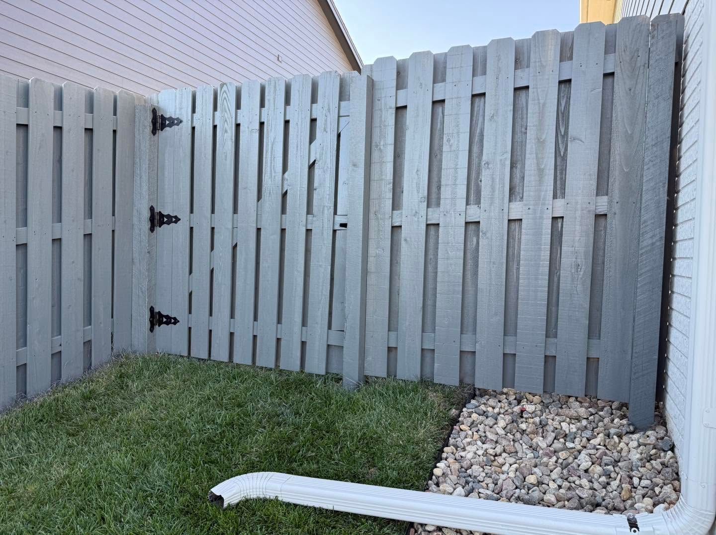 Gray wooden fence enclosing a small yard with grass and a gravel corner
