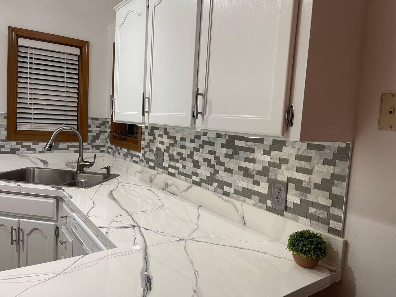 Modern kitchen with white cabinets, marble countertop, gray tile backsplash, and sink by a window