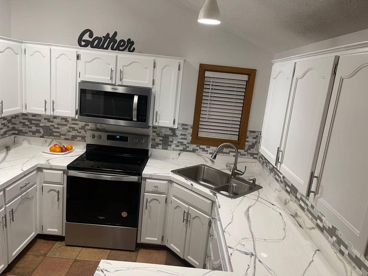 White kitchen with black appliances, marble counters, and a “Gather” sign above the microwave.