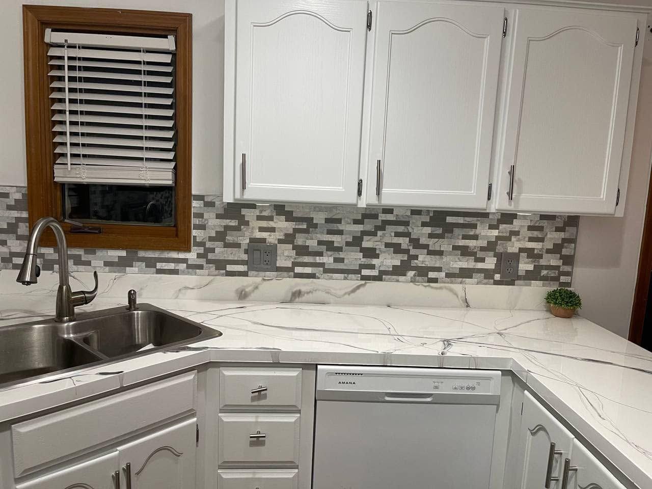 Bright white kitchen corner with sink, tiled backsplash, white cabinets, and a window with blinds