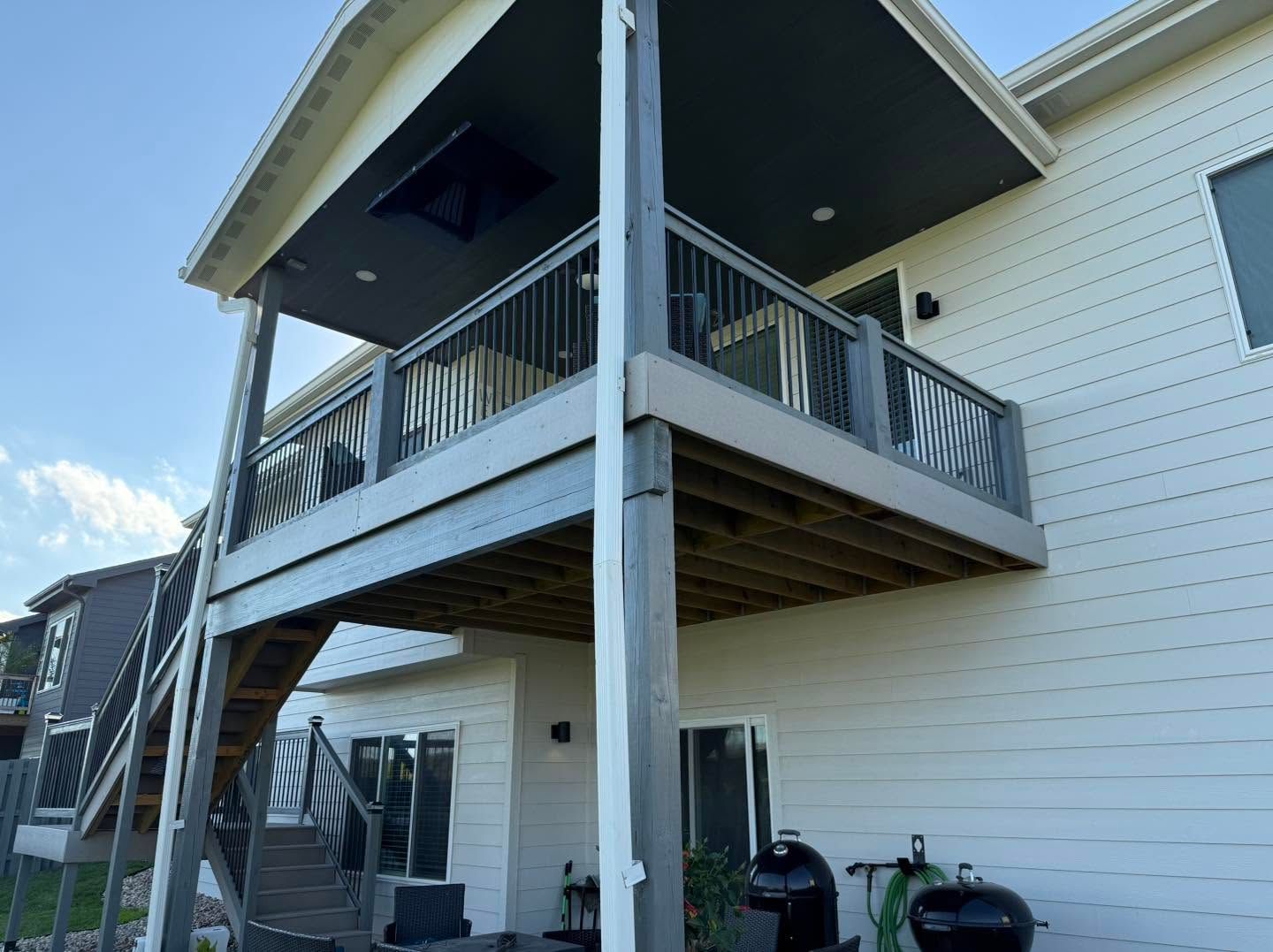 White two-story house with an elevated wooden deck and stairs, viewed from below