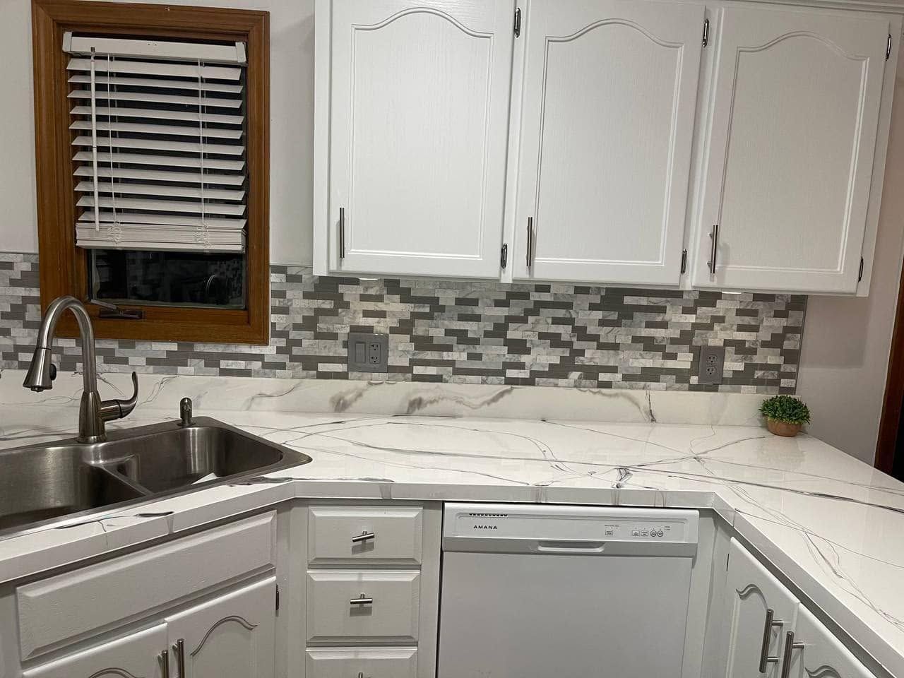 Modern white kitchen with stainless sink, mosaic backsplash, and cabinets above a dishwasher.