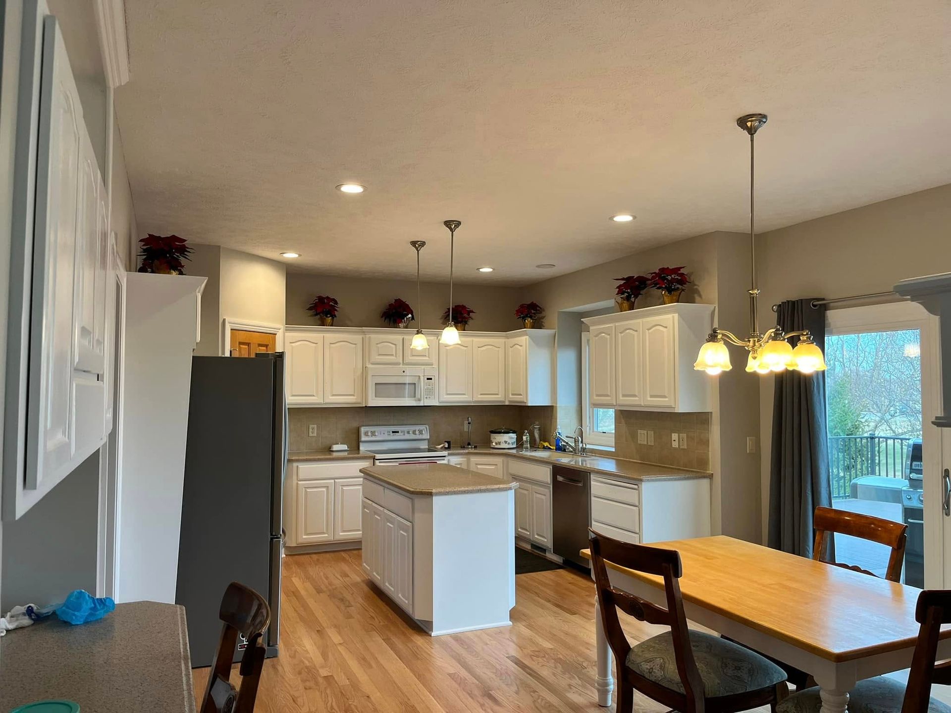 Bright, open kitchen and dining area with white cabinets, gray walls, and a wooden table by a window.