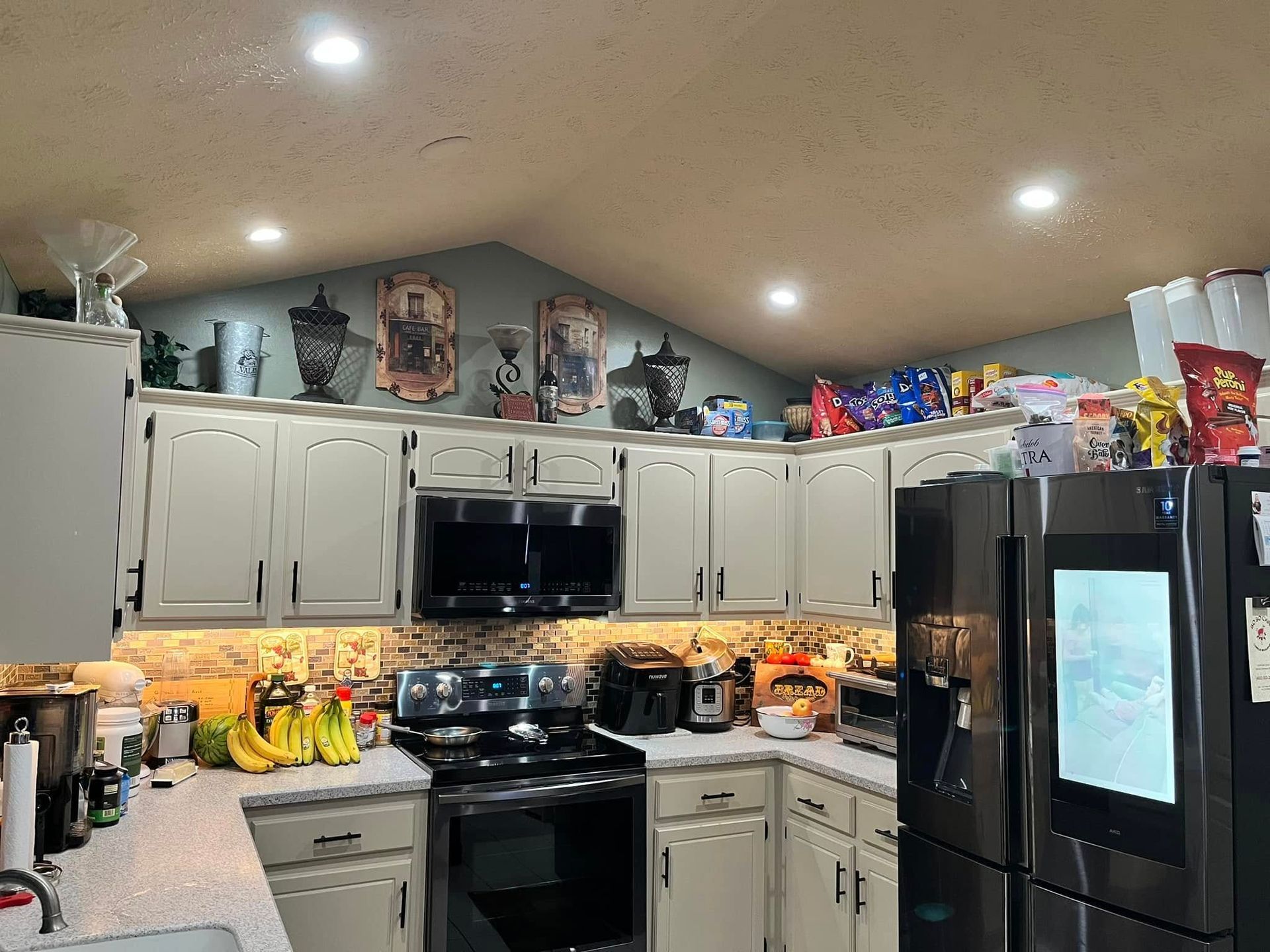 Bright kitchen with white cabinets, black appliances, and cluttered countertops under recessed lights