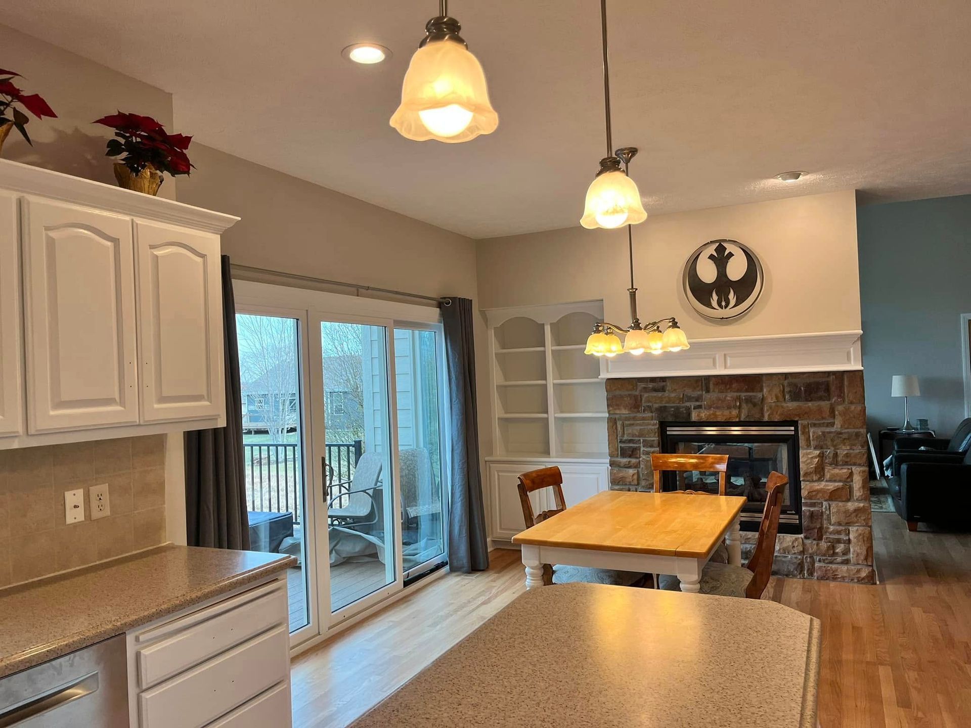 Bright kitchen with island, white cabinets, sliding glass door, and stone fireplace in an open dining area