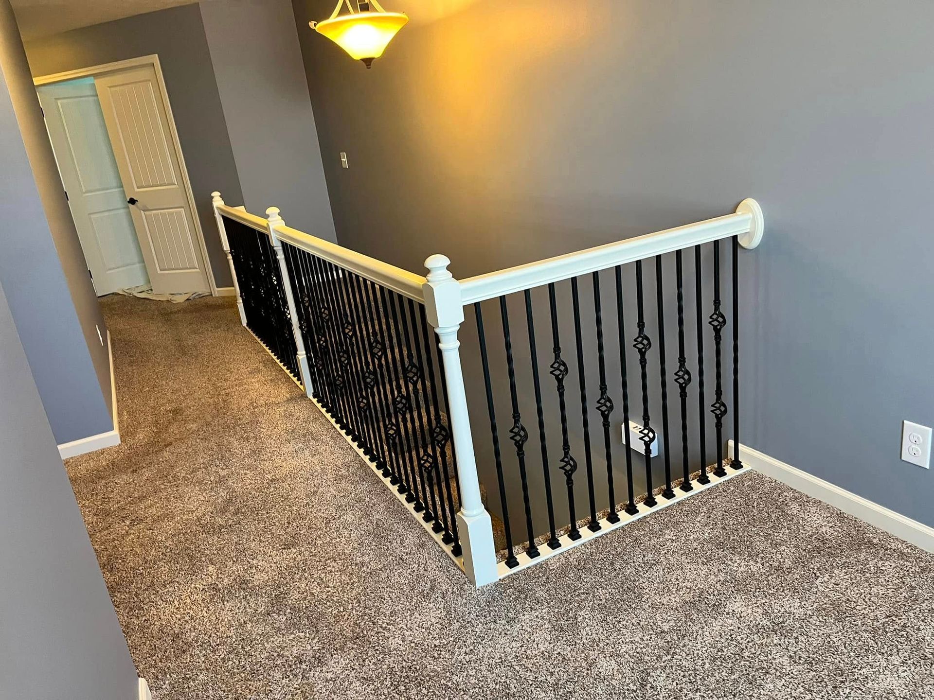 Hallway with gray walls, beige carpet, white banister, and black stair railing overlooking stairs